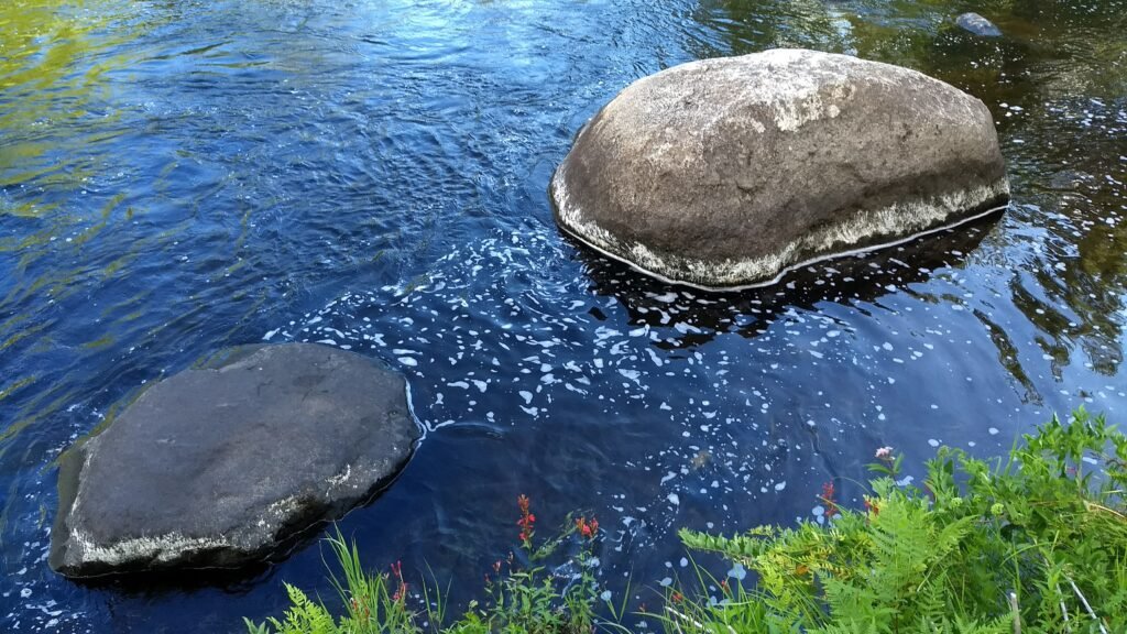 Two large boulders occupy a spot in a river, creating a bathing pool