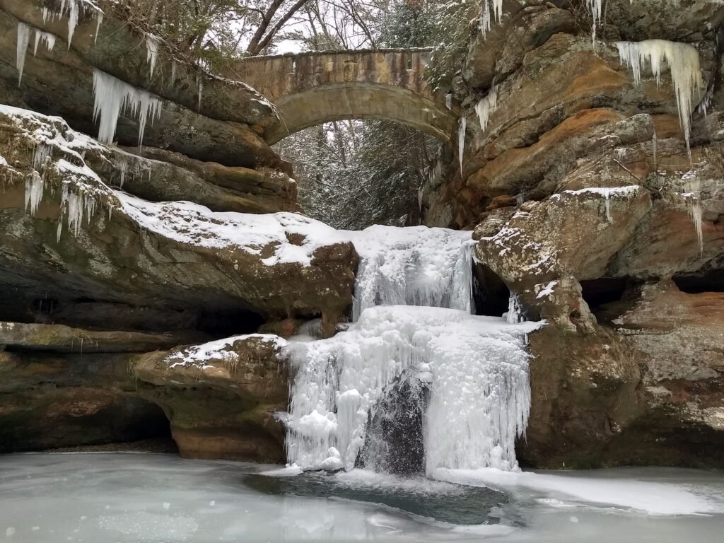 A bridge overlays a frozen waterfall, stuck in place in the middle of a horizontal bed of sandstone